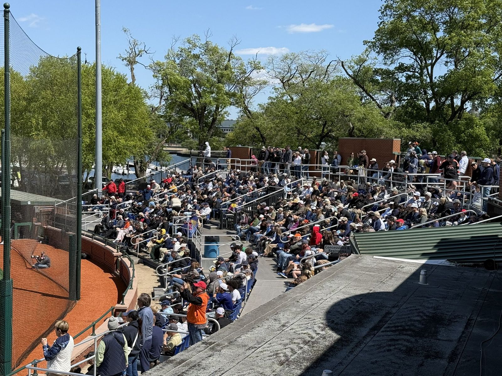 Packed bleachers behind the plate, shaded by the trees beyond the outfield
