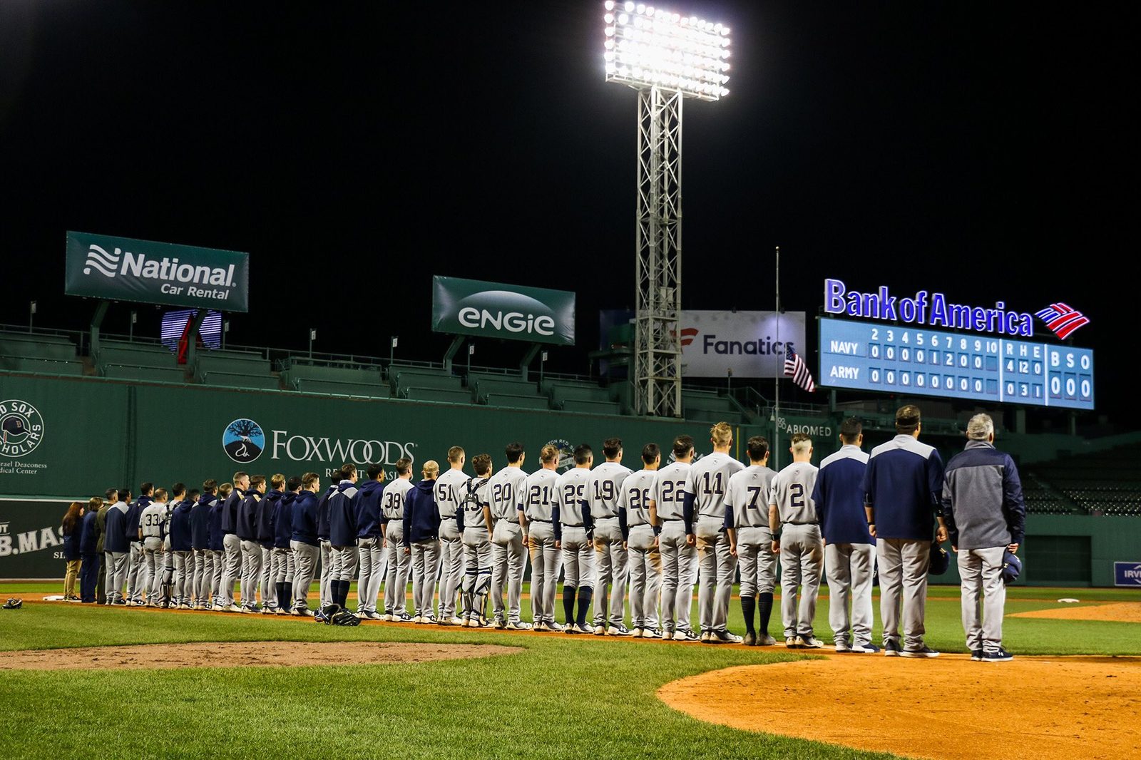 Navy lined up along the third-base line at Fenway Park under the lights, the scoreboard reading Navy 4 Army 0