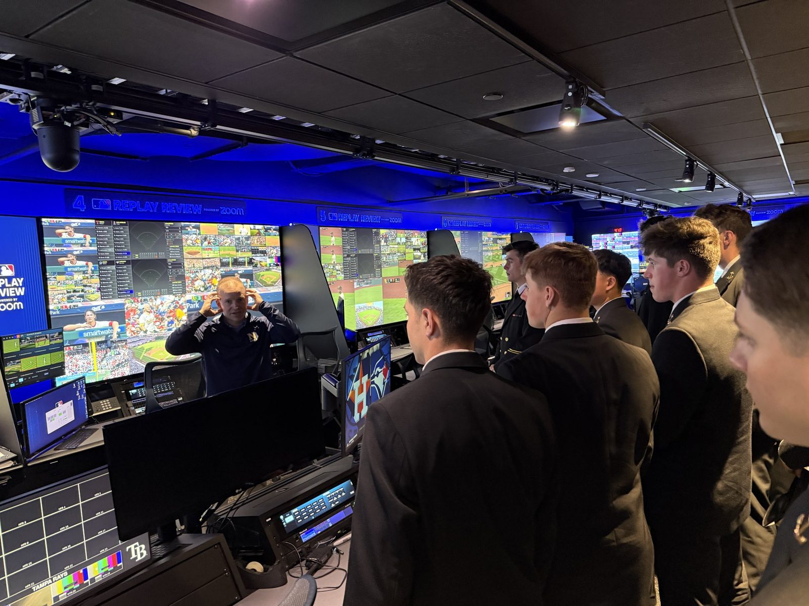 Midshipmen in dress blues inside MLB's Replay Operations Center, walls of live game monitors in front of them